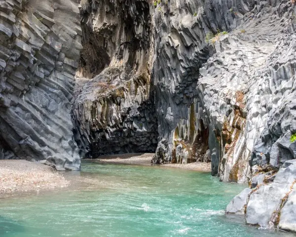 Acque cristalline scorrono tra le imponenti pareti basaltiche delle gole dell'Alcantara, creando una spiaggia naturale suggestiva.