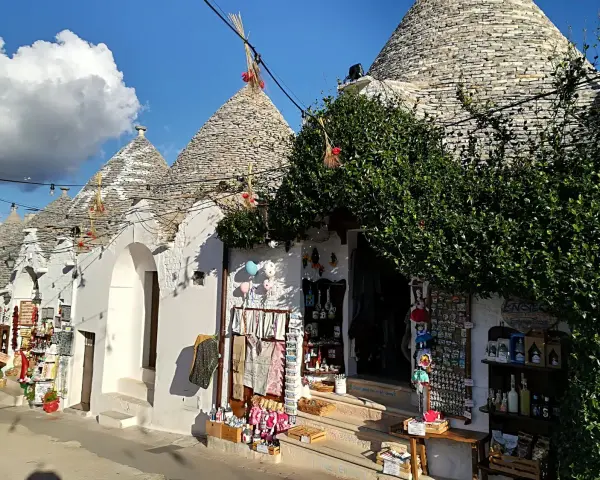 Trulli caratteristici della Valle d'Itria cosa vedere: negozi di souvenir con prodotti locali e decorazioni tipiche sotto un cielo azzurro.