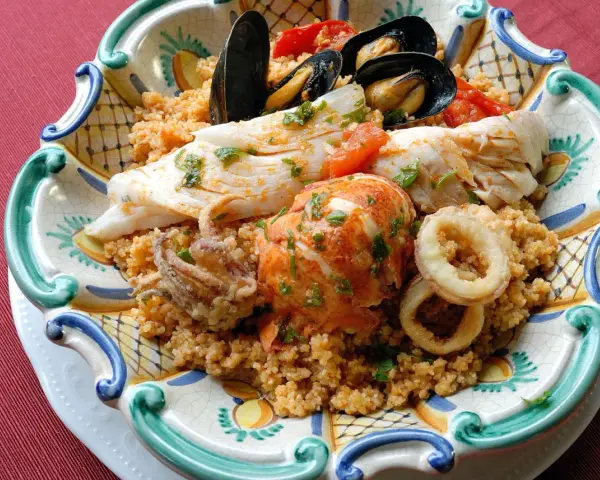 Piatto di pesce misto con couscous: ecco cosa mangiare a Trapani. Gamberi, calamari, pesce bianco e cozze.