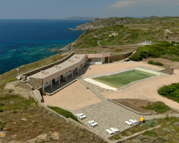 Un villaggio nurra affacciato sul mare turchese, con una piscina e lettini bianchi pronti per il relax.