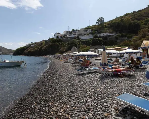 Spiaggia di ciottoli a Lipari, con lettini, ombrelloni e una barca all'ancora. La papesca beach è un luogo ideale per rilassarsi.