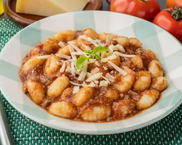 Gnocchi al ragù, un classico tra i piatti tipici di Perugia, serviti con parmigiano grattugiato e basilico fresco.