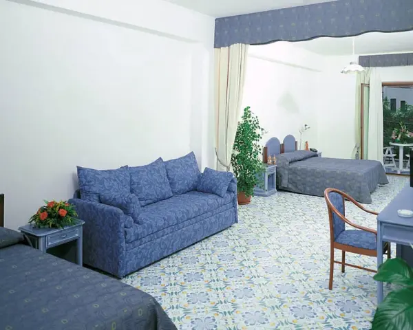 Camera spaziosa con divano blu, letti singoli e un letto matrimoniale. Pavimento decorato, tipico del **hotel club residence Martinica**.