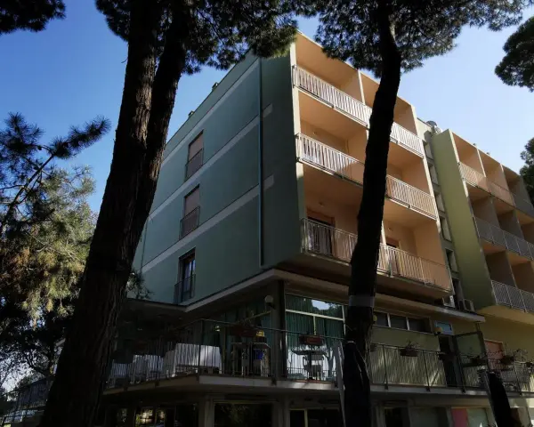 Edificio del pine beach hotel rosolina mare, con balconi e alberi di pino davanti.