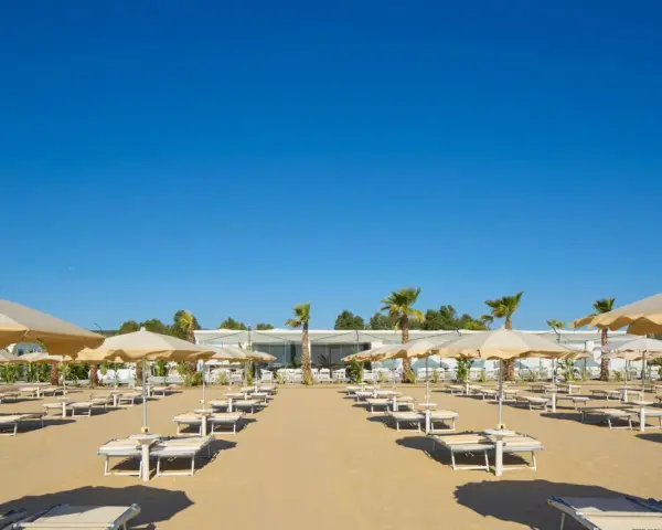 Filettate file di lettini e ombrelloni sulla sabbia dorata di Ripa Beach Vieste, sotto un cielo azzurro e limpido.