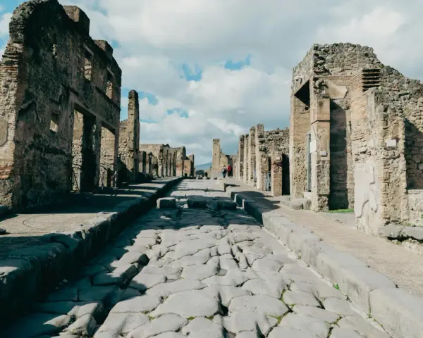 Antica strada romana a Pompei, con rovine di edifici e turisti che passeggiano. Un'ottima guida per come visitare Pompei.