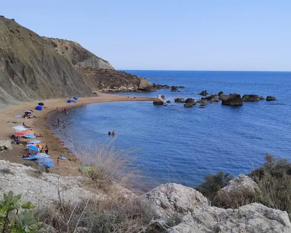 Spiaggia di Cala Vincenzina con scogliere, ombrelloni colorati e bagnanti che si godono il mare azzurro.