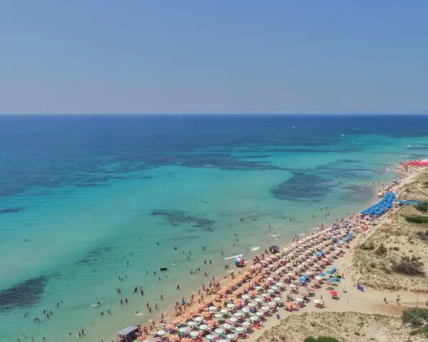 Spiaggia affollata con ombrelloni colorati e gente che nuota nelle acque cristalline di Punta Prosciutto, le Maldive del Salento.