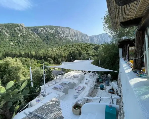 Terrazza panoramica con vista sui monti di Oliena, Sardegna. Arredamento bianco, cactus e vegetazione rigogliosa.