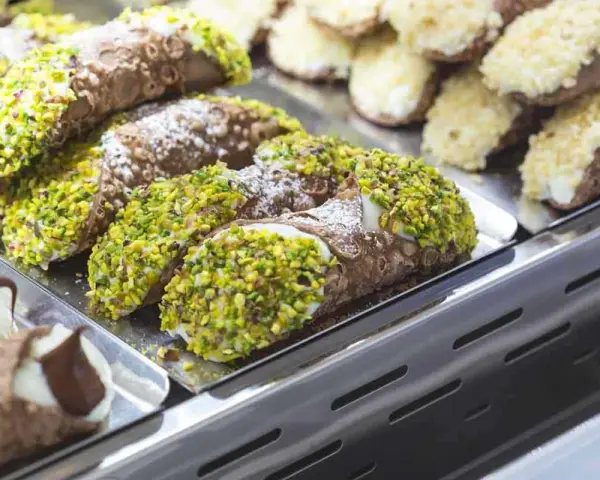 Cannoli siciliani, dolci tipici siciliani, ricoperti di pistacchi e zucchero a velo, in una vetrina.