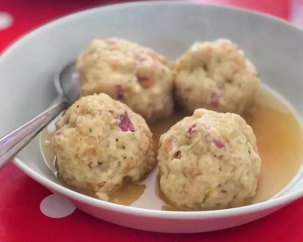 Canederli in brodo, un classico dei piatti tipici trentino alto adige, serviti in una ciotola bianca su un tovagliolo rosso a pois bianchi.