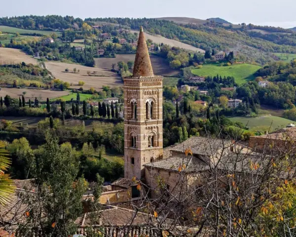 Campanile in borgo marchigiano, tra colline verdi e campi dorati, ideale per itinerari Marche autunnali.