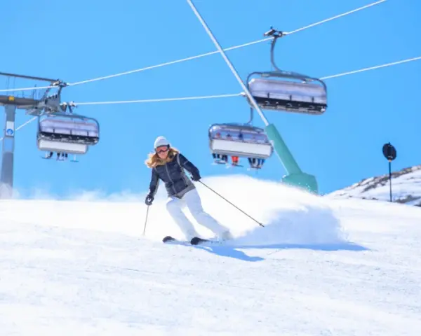 Donna scia su pendio innevato, con seggiovie sullo sfondo. Perfetta per la tua settimana bianca dove andare.