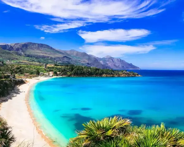 Una baia incantevole con acque cristalline e sabbia dorata, tra le spiagge più belle in Sicilia. Montagne verdi sullo sfondo.
