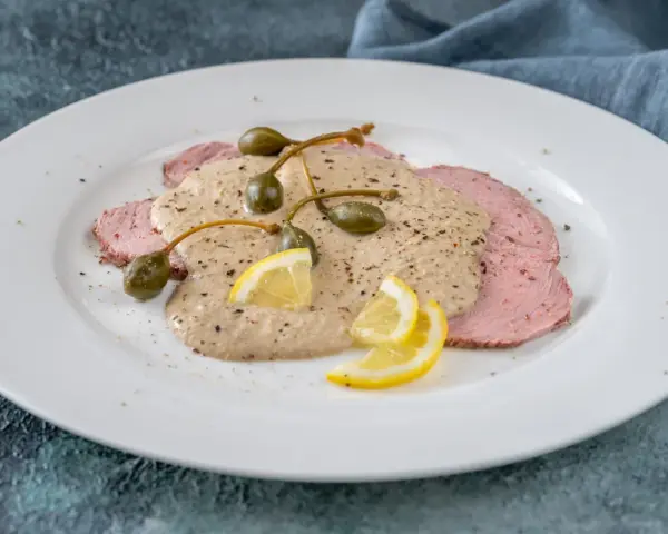 Vitello tonnato, uno dei piatti tipici di Torino, con fettine di carne rosa, salsa cremosa, capperi e limone.