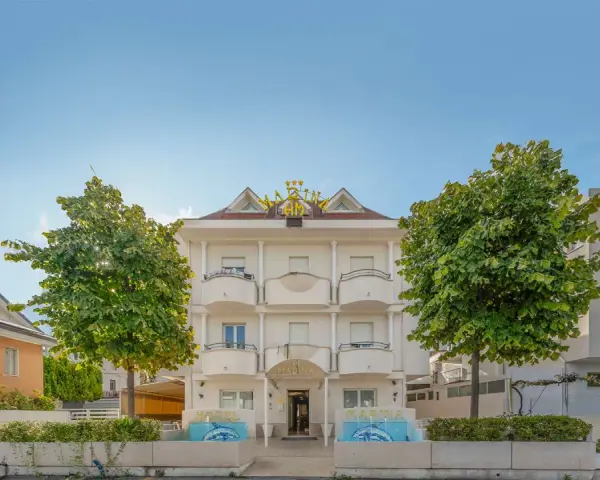 Hotel Marina Riccione: facciata bianca con insegna dorata, alberi verdi e fontane. Le recensioni lo descrivono come un'ottima scelta.