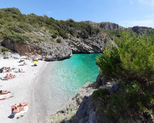 Spiaggia di ciottoli con gente che prende il sole e acque cristalline nel **Cilento mare**.