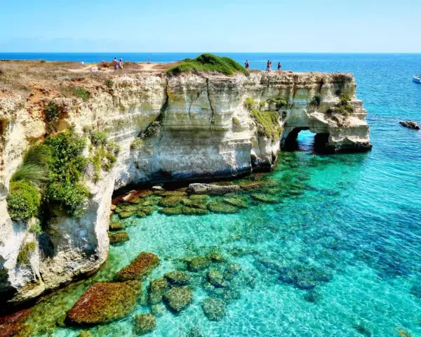 Scogliere bianche e mare cristallino sul litorale adriatico. Turisti ammirano il panorama, un catamarano naviga in lontananza.