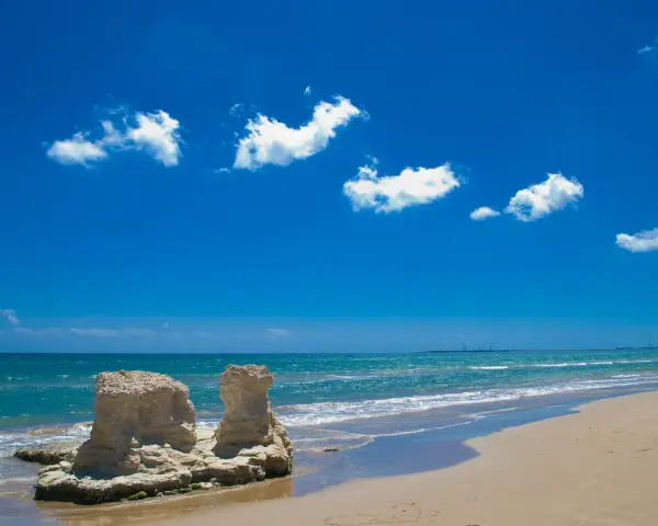 Spiagge bianche in Sicilia, con rocce scolpite dal mare e un cielo azzurro pieno di nuvole bianche.