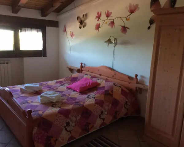 Camera accogliente in un agriturismo al Selvadigo, con letto, coperta colorata, cuscino rosa e decorazioni a farfalle e fiori sul muro.