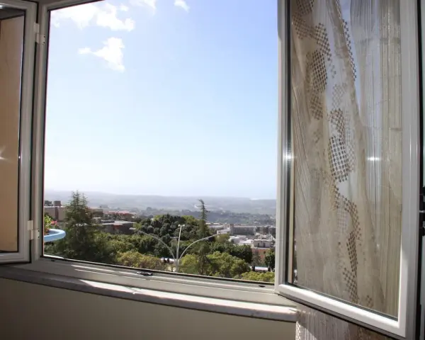 La terrazza sulla valle offre una vista panoramica su un paesaggio collinare con case e alberi verdi sotto un cielo azzurro.