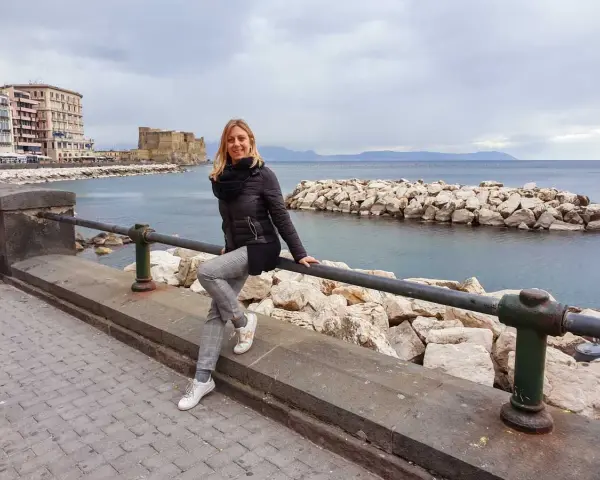 Donna sorridente sul lungomare di Napoli, con Castel dell'Ovo sullo sfondo. Perfetto per scoprire cosa vedere a Napoli in 3 giorni.