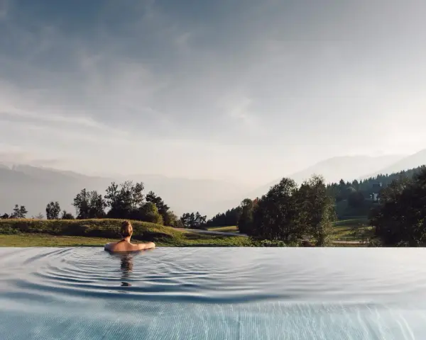 Donna rilassata in piscina a sfioro con vista sulle montagne, un'esperienza indimenticabile all'hotel Milla Montis.
