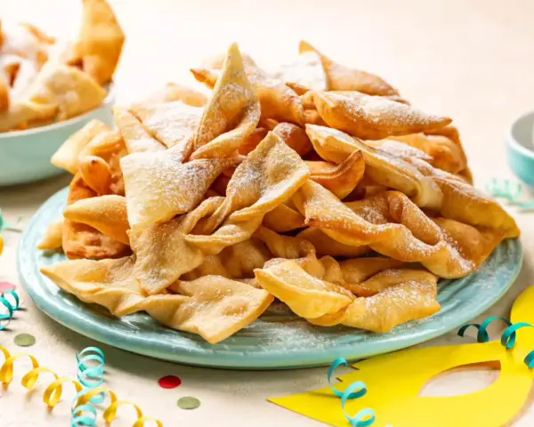 Dolci fritti a forma di fiocco, cosparsi di zucchero a velo, sono un classico di cosa si mangia a Carnevale in Italia.