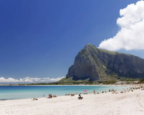 Spiaggia di San Vito Lo Capo, Sicilia, con il Monte Monaco imponente sullo sfondo e il mare cristallino che invita a un bagno.