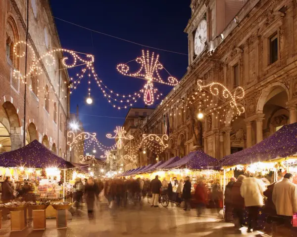 Una strada illuminata da lucine natalizie, con bancarelle e gente che passeggia: ecco i mercatini di Natale più belli.