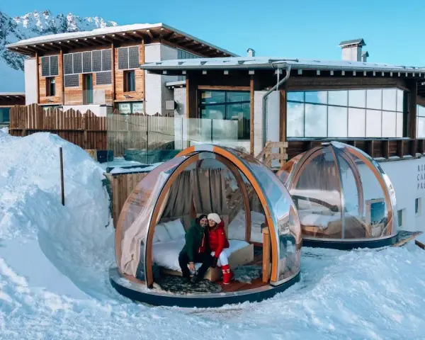 Coppia in una bolla trasparente innevata, perfetta idea su dove andare a gennaio in Italia per un soggiorno da sogno tra le montagne.