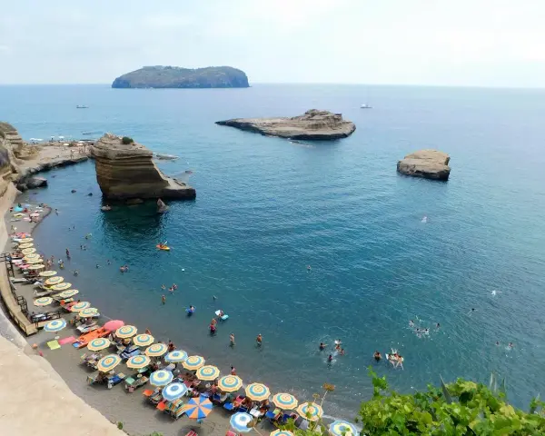 Le **spiagge** di Ventotene, con ombrelloni colorati e bagnanti in un mare azzurro, fanno da cornice a scogli suggestivi e all'isola di Santo Stefano in lontananza.