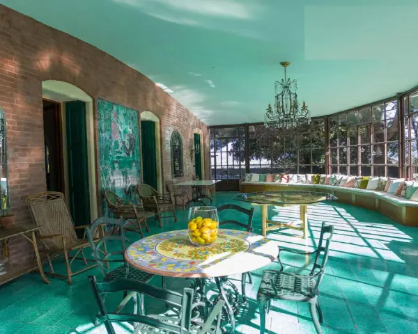 Veranda luminosa della villa dei cipressi a Sona, con pavimenti verdi, mobili in vimini e un grande divano curvo con cuscini colorati.