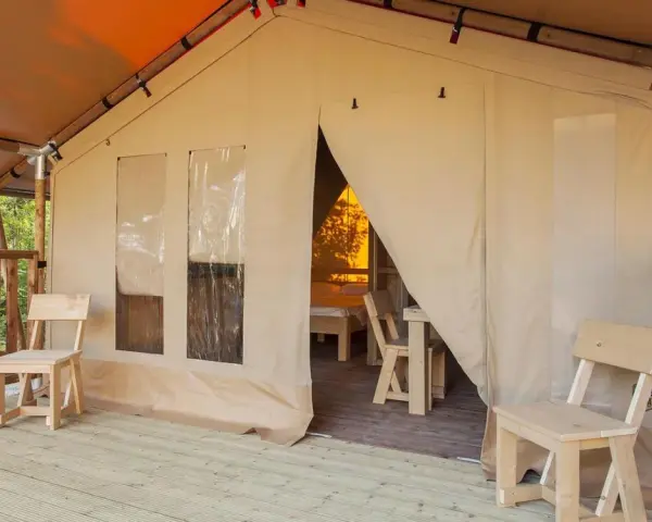 Tenda accogliente nel Luxor Chianti Glamping Village, con sedie in legno sulla veranda e vista sull'interno arredato.