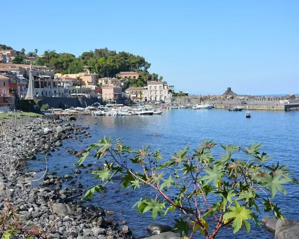 Il lungomare di Acireale, con case colorate, barche ormeggiate e il mare azzurro.
