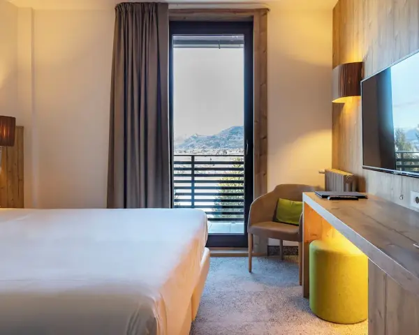 Camera accogliente con vista panoramica, tipica del Linta Hotel Asiago. Letto comodo, poltrona e balcone con paesaggio montano.