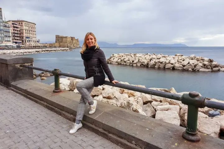Donna sorridente sul lungomare di Napoli, con Castel dell'Ovo sullo sfondo. Perfetto per scoprire cosa vedere a Napoli in 3 giorni.