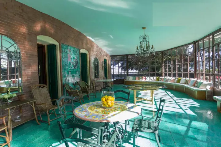 Veranda luminosa della villa dei cipressi a Sona, con pavimenti verdi, mobili in vimini e un grande divano curvo con cuscini colorati.