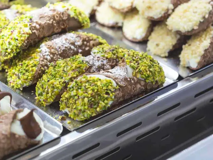 Cannoli siciliani, dolci tipici siciliani, ricoperti di pistacchi e zucchero a velo, in una vetrina.