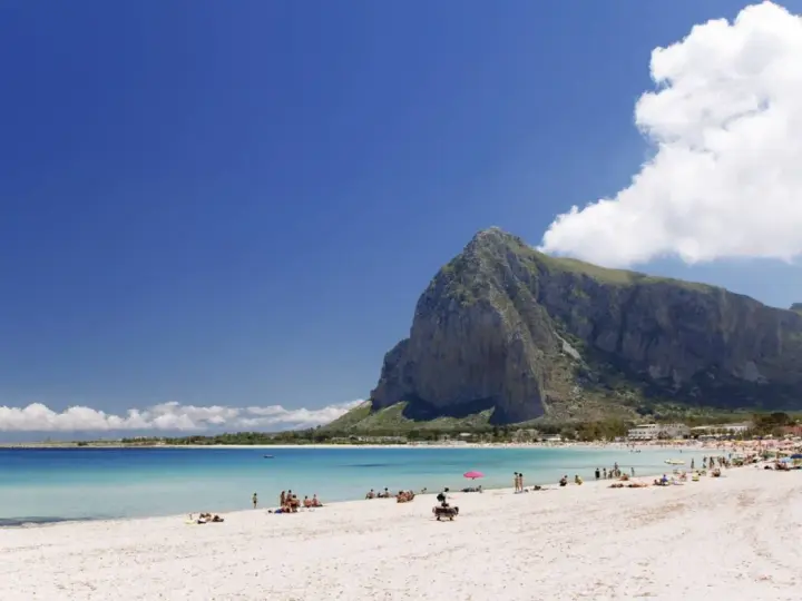 Spiaggia di San Vito Lo Capo, Sicilia, con il Monte Monaco imponente sullo sfondo e il mare cristallino che invita a un bagno.