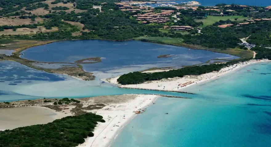 Vista aerea della spiaggia La Cinta con acque turchesi, lagune interne e vegetazione lussureggiante.