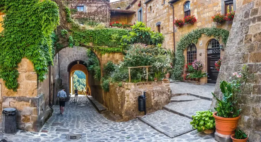 Un vicolo acciottolato tra antiche case in pietra, ricoperte di edera e fiori. Un invito a scoprire i borghi da visitare nelle Marche.