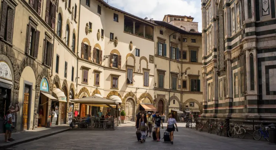 Un gruppo di turisti con valigie a rotelle cammina in una piazza fiorentina, un'immagine perfetta per un **viaggio in Toscana**.