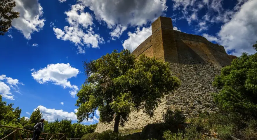 Roccia imponente e cielo azzurro con nuvole bianche: ecco cosa vedere a Pomarance, con un escursionista che ammira la fortezza.