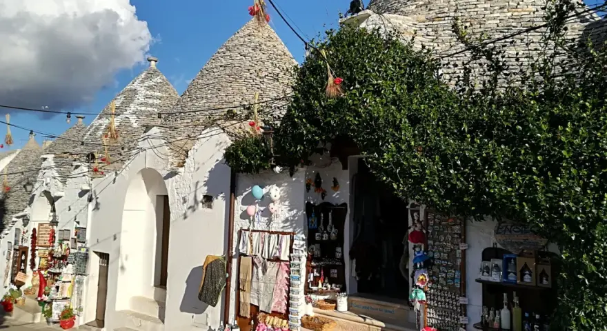 Trulli caratteristici della Valle d'Itria cosa vedere: negozi di souvenir con prodotti locali e decorazioni tipiche sotto un cielo azzurro.