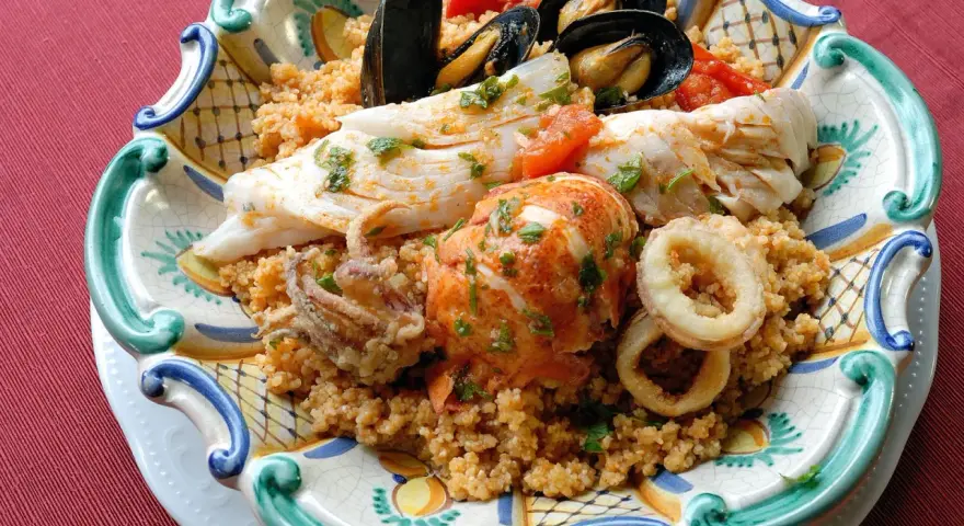 Piatto di pesce misto con couscous: ecco cosa mangiare a Trapani. Gamberi, calamari, pesce bianco e cozze.