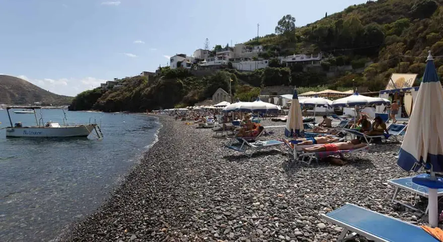 Spiaggia di ciottoli a Lipari, con lettini, ombrelloni e una barca all'ancora. La papesca beach è un luogo ideale per rilassarsi.