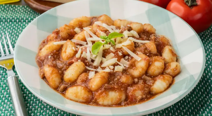 Gnocchi al ragù, un classico tra i piatti tipici di Perugia, serviti con parmigiano grattugiato e basilico fresco.