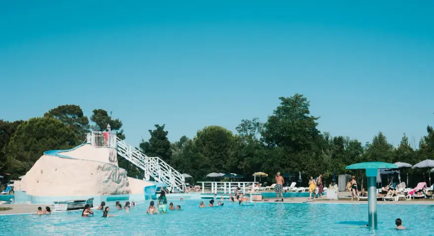 Bambini e adulti si divertono nella piscina del villaggio Ca' Laguna, con scivoli e zone relax sotto il sole.