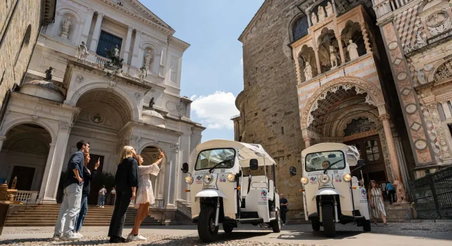 Tuk-tuk turistici pronti per esplorare cosa vedere a Bergamo in un giorno. Turisti scattano foto davanti a splendidi edifici storici.